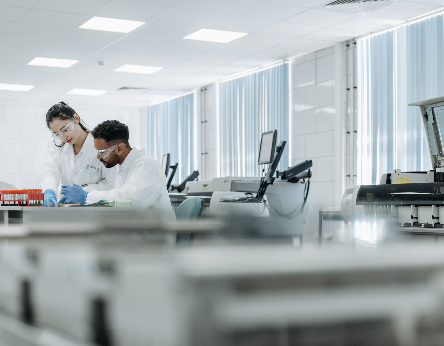 Two scientists working in a high-tech laboratory setting, wearing protective eyewear and gloves.